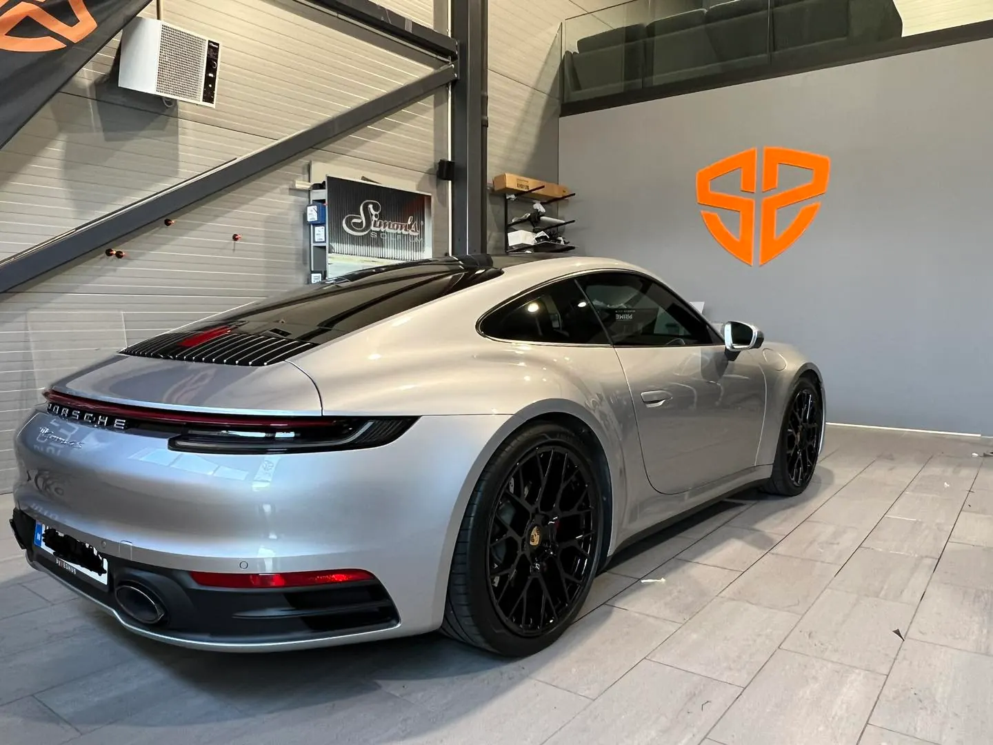 Sølvgrå Porsche 911 i Simons verksted med orange SS-logo på vegg